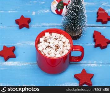 hot chocolate with marshmallow in a red ceramic mug on a blue wooden background and festive decor, top view