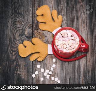hot chocolate with marshmallow in a red mug on a gray wooden background and carnival deer&rsquo;s hat, top view
