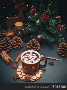 hot chocolate with marshmallows in a brown mug on a black background, behind a christmas decor