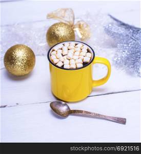 hot chocolate with marshmallows in a yellow cup and Christmas toys on a white wooden background