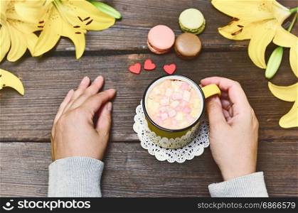 Hot chocolate with marshmallows in female hands on a brown table, top view