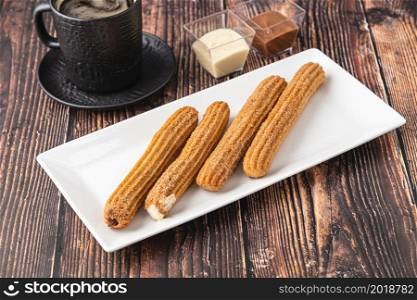 Hot churros with chocolate sauce on wooden table