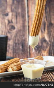 Hot churros with chocolate sauce on wooden table.