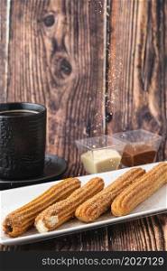 Hot churros with chocolate sauce on wooden table.