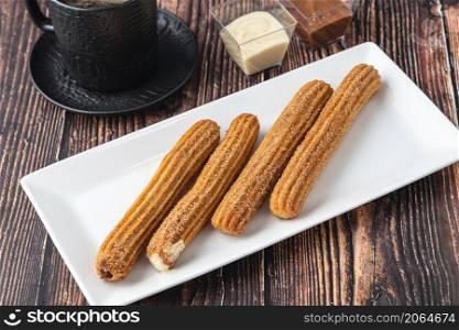 Hot churros with chocolate sauce on wooden table.