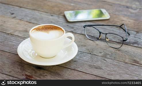Hot coffee, glasses, and smartphone on a wooden table.