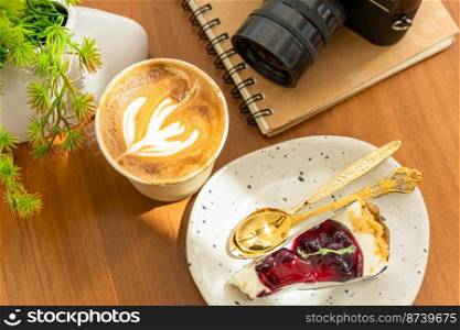 Hot coffee latte with latte art milk foam in cup made of paper and camera in notebook ,Blueberry Cake on wood desk on top view. As breakfast In a coffee shop at the cafe,during business work concept