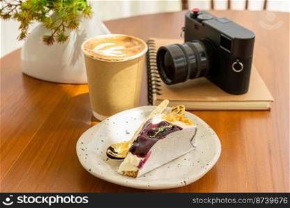 Hot coffee latte with latte art milk foam in cup made of paper and camera in notebook ,Blueberry Cake on wood desk on top view. As breakfast In a coffee shop at the cafe,during business work concept