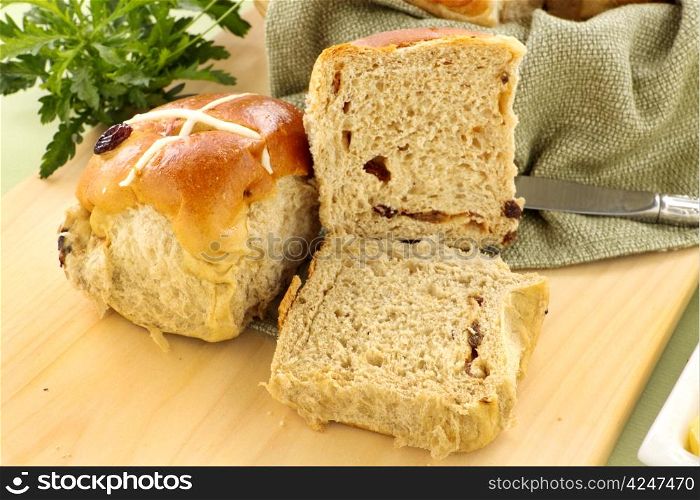 Hot cross buns with sliced open on a bread board.