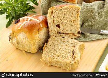 Hot cross buns with sliced open on a bread board.