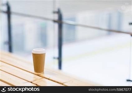 hot drink, winter and leisure concept - close up of coffee cup on wooden bench at skating rink