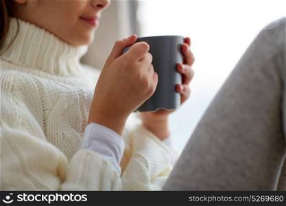 hot drinks and people concept - beautiful girl in winter sweater with tea mug sitting at home window. girl with tea mug sitting at home window