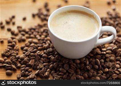 hot drinks concept - close up coffee cup and roasted beans on wooden table. close up coffee cup and beans on wooden table