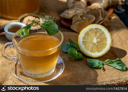 Hot Ginger juice with lemon and mint, root and slices of ginger Served with brown sugar and honey on sackcloth background. Hot ginger juice can helps warming body, Healthy Drink.