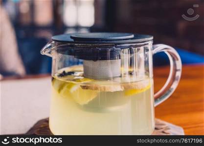 Hot herbal tea is in a glass kettle on the tabletop in cafeteria. On the surface of the drink float pieces of ginger, lemon and cinnamon.. herbal tea is in a glass kettle.