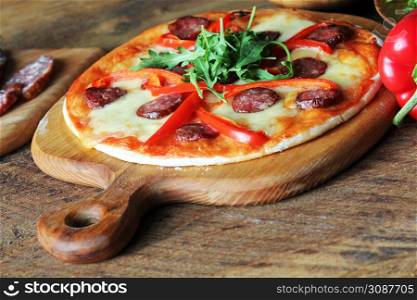Hot homemade pizza with Pepperoni, paprica, rucola on wooden table .. Hot homemade pizza with Pepperoni, paprica, rucola on wooden table