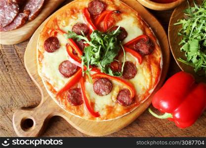 Hot homemade pizza with Pepperoni, paprica, rucola on wooden table . Top view .. Hot homemade pizza with Pepperoni, paprica, rucola on wooden table. Top view