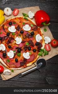 Hot italian pizza on dark wooden table with ingredients and cutter