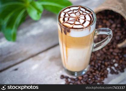 Hot latte macchiato coffee with chocolate syrup art on top,wooden table background.