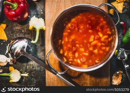 Hot Mexican spicy soup in cooking pot with ladle on rustic kitchen table background, top view.