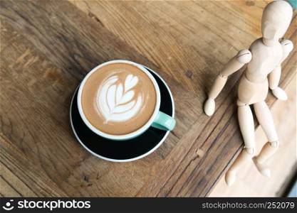 Hot mocha coffee or capuchino in the green cup with a wood man sitting on the wooden table