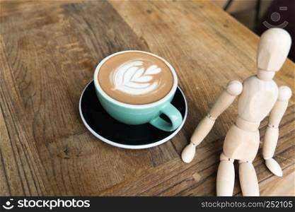 Hot mocha coffee or capuchino in the green cup with a wood man sitting on the wooden table