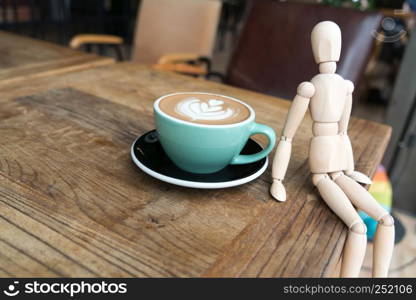 Hot mocha coffee or capuchino in the green cup with a wood man sitting on the wooden table