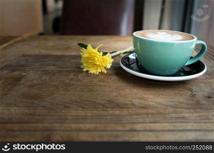 Hot mocha coffee or capuchino in the green cup with heart pattern and yellow flower on the wooden table