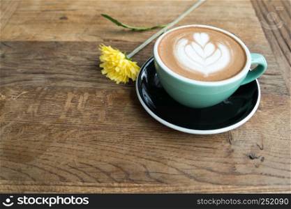 Hot mocha coffee or capuchino in the green cup with heart pattern and yellow flower on the wooden table