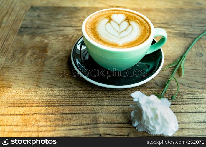 Hot mocha coffee or capuchino with heart pattern and white carnation flower on the wooden table