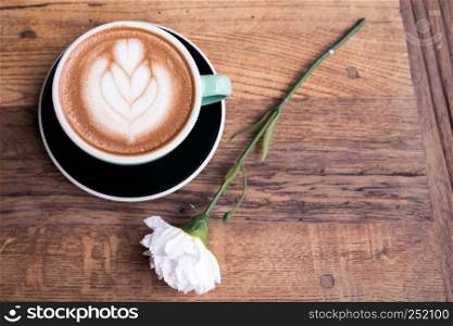 Hot mocha coffee or capuchino with heart pattern and white carnation flower on the wooden table