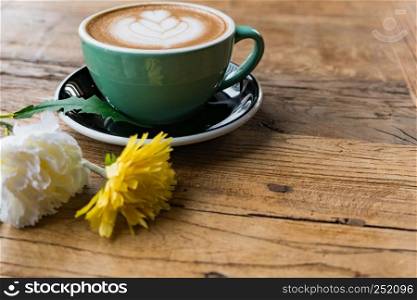 Hot mocha coffee or capuchino with heart pattern and yellow flower and white carnation on the wooden table