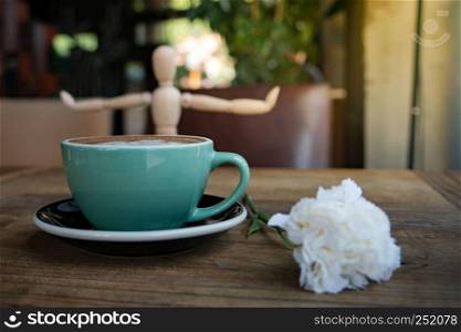 Hot mocha coffee or capuchino with white carnation flower and wood man on the wooden table