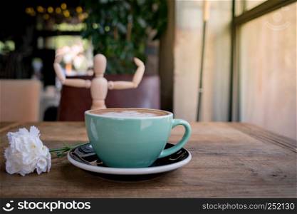 Hot mocha coffee or capuchino with white carnation flower and wood man on the wooden table