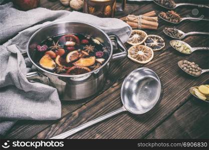 hot mulled wine in a pot with handles and an iron kitchen scoop on a brown wooden background, vintage toning