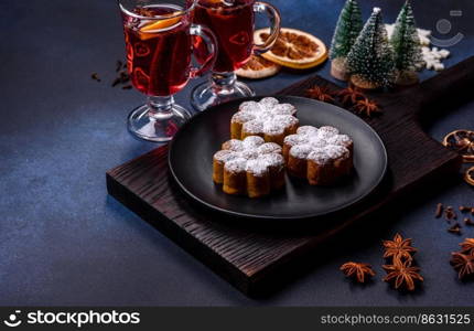 Hot mulled wine with a slice of orange, with cinnamon, cloves and other spices with chocolate muffins and Christmas decorations on a dark concrete background. Hot mulled wine with a slice of orange, with cinnamon, cloves and other spices