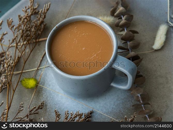 Hot orange milk tea in a blue ceramic cup, Sweet refreshment thai milk tea on ceramic and dried flowers on ceramic plate. Selective focus.