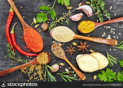 Hot pepper, ginger, fenugreek, turmeric in spoons, nutmeg, cardamom, star anise and coriander, rosemary, parsley, thyme, garlic and chili pods on black wooden board top