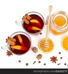 Hot red mulled wine, bee honey, slices of oranges and spices isolated on white background. Flat lay, top view. Free space for text.