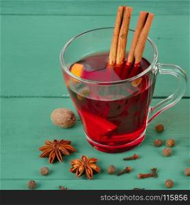 Hot red mulled wine on wooden background with spices, orange slice, anise and cinnamon sticks, close up.