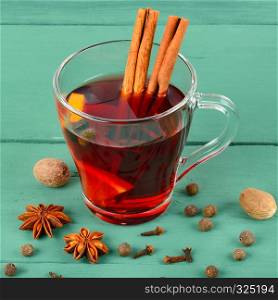 Hot red mulled wine on wooden background with spices, orange slice, anise and cinnamon sticks, close up.