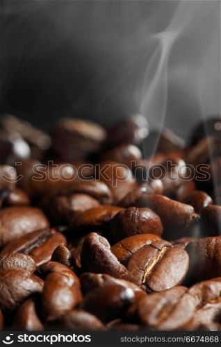 Hot roasted coffee beans and steam on black. Hot roasted coffee beans
