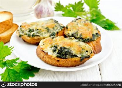 Hot sandwiches with nettles and cheese on slices of wheat bread in a plate, garlic on a wooden board background