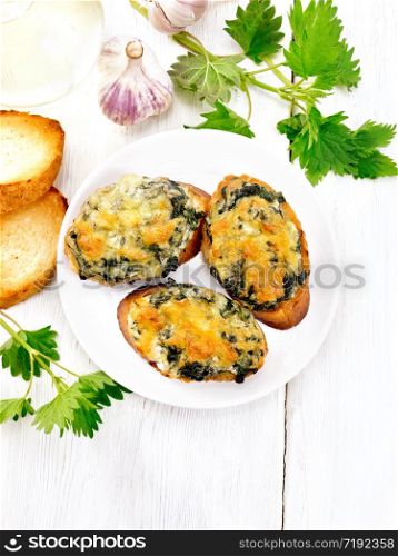 Hot sandwiches with nettles and cheese on slices of wheat bread in a plate on the background of a light wooden board from above