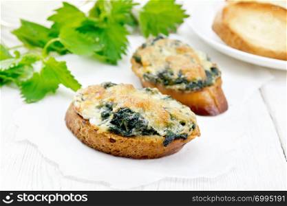 Hot sandwiches with nettles and cheese on slices of wheat bread on parchment against the background of light wooden boards