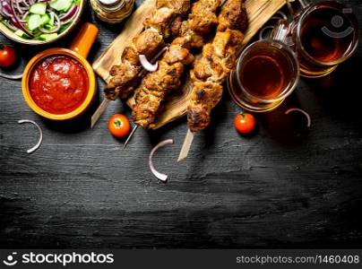 Hot Shish kebab with a cold beer. On the black wooden table.. Hot Shish kebab with a cold beer.