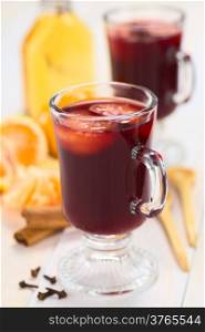 Hot spiced mulled red wine with mandarin on top, with cloves, cinnamon sticks, mandarin, wooden spoon and a small bottle of rum (Selective Focus, Focus on the front of the rim and the handle of the glass)