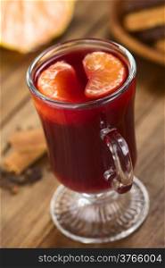 Hot spiced mulled red wine with mandarin segments on top, with cloves and cinnamon on the side, cookies in the back (Selective Focus, Focus on the front of the right mandarin segment on the drink)