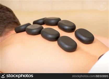 Hot stone massage therapy. Caucasian young man getting a hot stone massage on back at spa salon. Hot stone massage therapy. Caucasian young man getting a hot stone massage on back at spa salon.