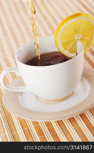 Hot tea being poured from a teapot into a cup with lemon